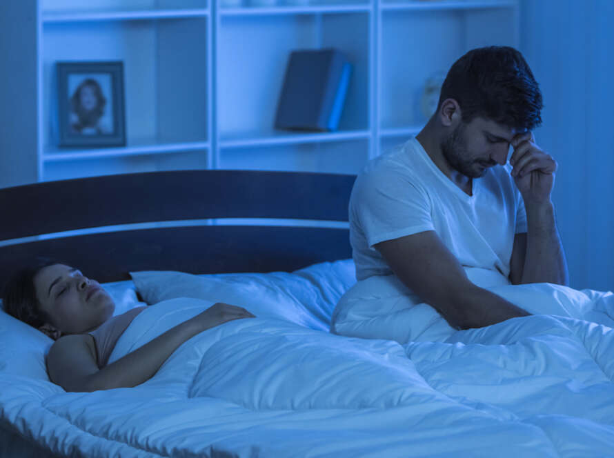 The man with a headache sit in the bed. night time